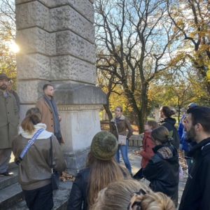 a group of people standing around a tour guide in a cemetery on a fall day