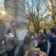 a group of people standing around a tour guide in a cemetery on a fall day