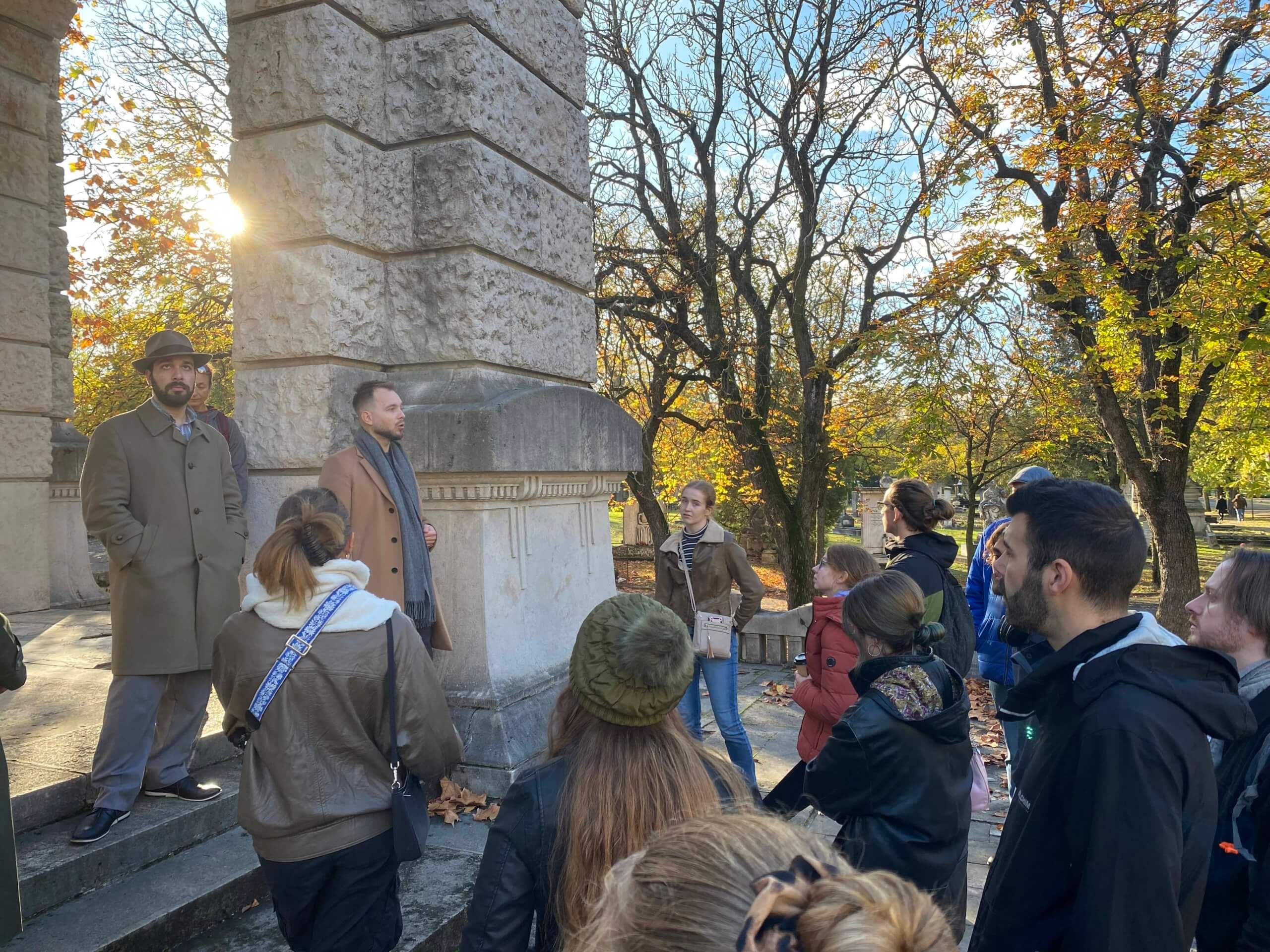 a group of people standing around a tour guide in a cemetery on a fall day